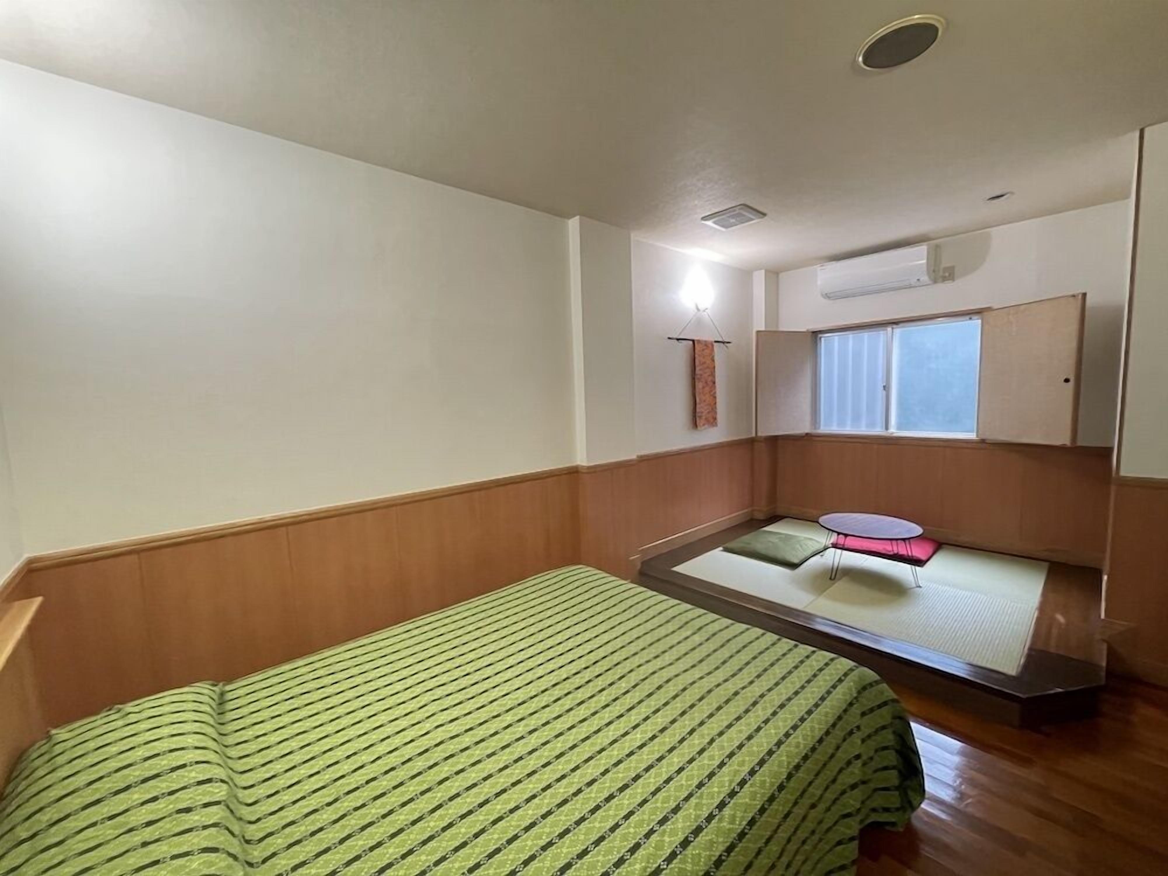 Una habitación pequeña y ordenada, con cama, una mesita y una ventana.