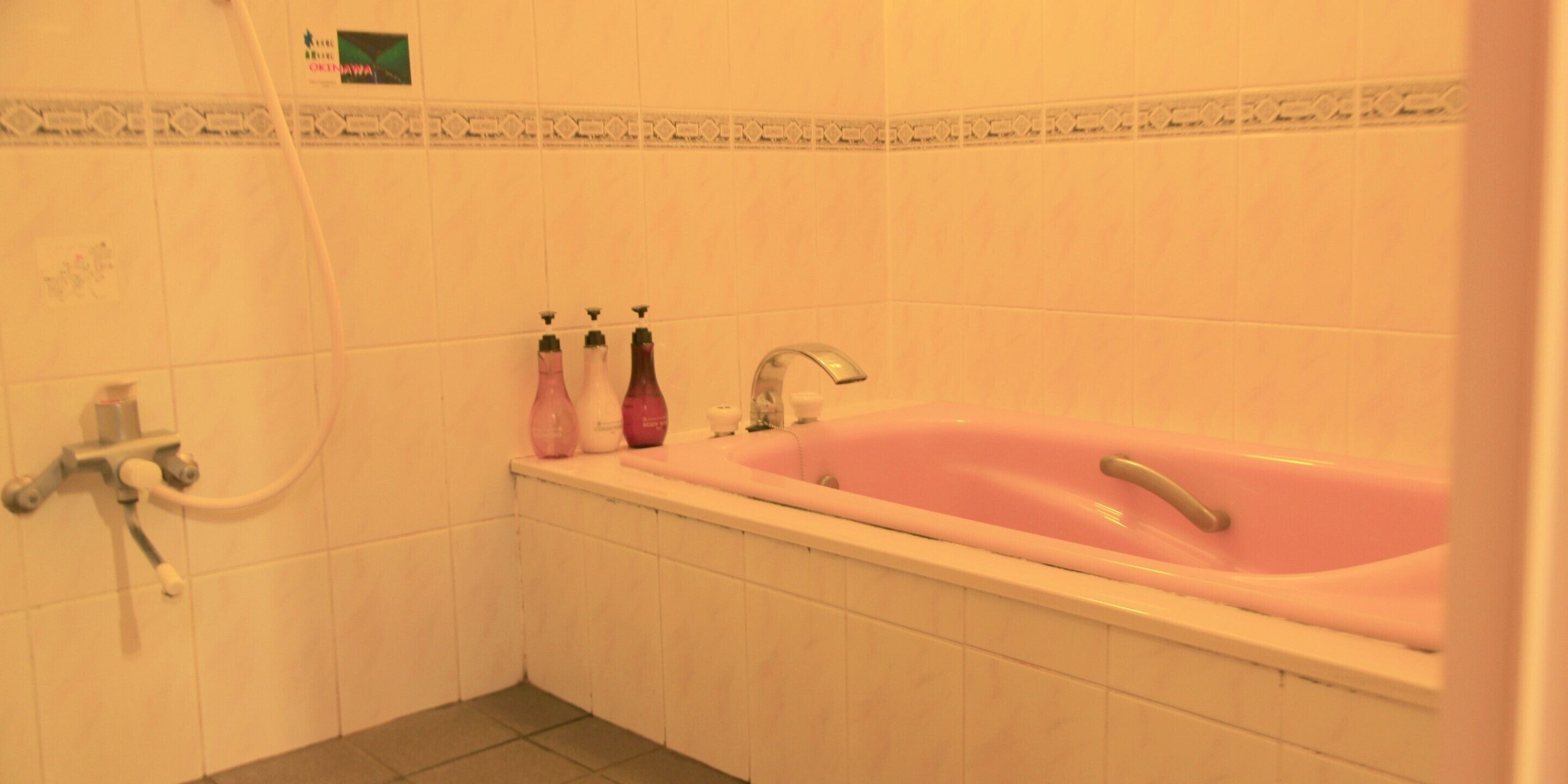 A bathroom with a pink bathtub, a shower, and three bottles of shampoo on the sink.