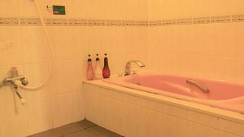 A bathroom with a pink bathtub, a shower, and three bottles of shampoo on the sink.