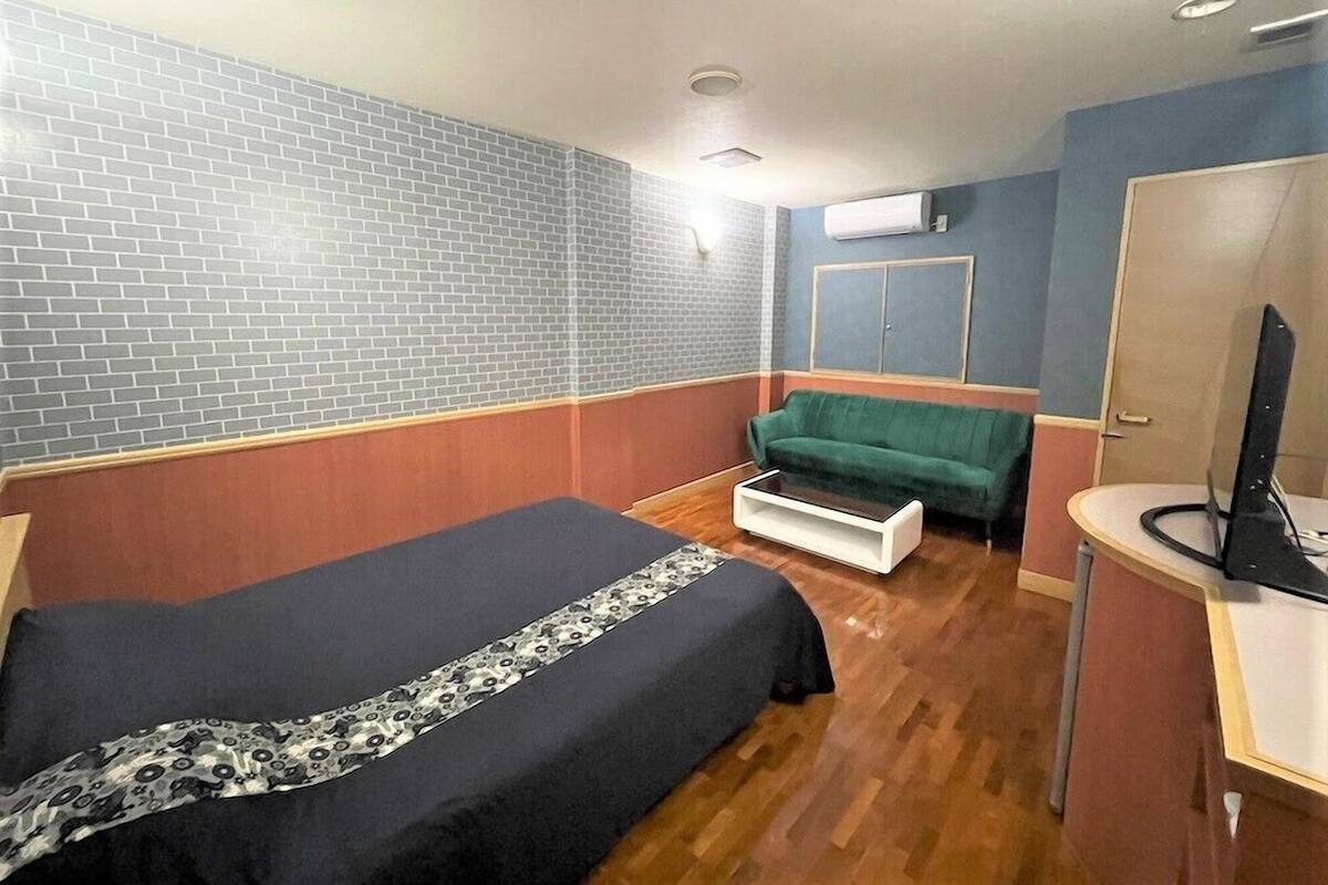 Una habitación de hotel con una cama, un sofá verde, una mesita, un espejo y un equipo de aire acondicionado en la pared.