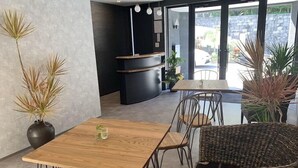 A modern interior with a reception desk, wooden tables, wicker chairs, and potted plants. - Hotel Bin (Okinawa)