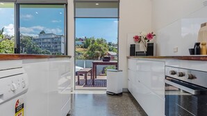 Una cocina moderna con armarios blancos, un horno negro y vistas a un balcón con mesa y sillas.