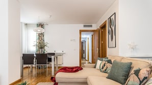 Uma sala de estar moderna com um sofá, uma área de jantar com mesa e cadeiras, e uma cozinha ao fundo.