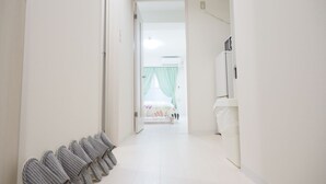 Un corridoio con un letto sullo sfondo, una fila di ciabatte e un muro bianco con una presa di corrente.