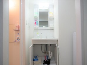 Une salle de bain avec un lavabo blanc, un miroir et une étagère contenant des articles de toilette.