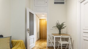 Ein Flur mit Holzboden, einem Sofa mit gelber Decke, einem kleinen Tisch mit Stühlen und einer Tür zu einem anderen Raum.