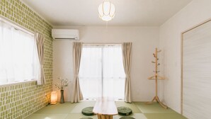 A room with tatami mats, a wooden table, a hanging light fixture, a coat rack, and a window with curtains. - Sea Sunset Villa (Motobu)
