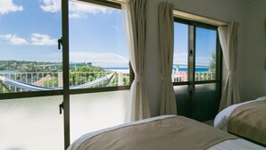 A hotel room with a large window, a view of a bridge, and a hammock outside. - Sea Sunset Villa (Motobu)
