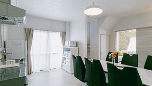 A modern kitchen with a dining area, white appliances, and a large window with curtains. - Sea Sunset Villa (Motobu)