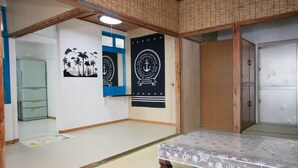 Ein Zimmer mit Tatami-Boden, einem Futon-Bett, einem Holzschrank und zwei schwarzen Bannern mit Meeresmotiven.