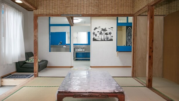Ein traditioneller japanischer Raum mit Tatami-Böden, einem niedrigen Holztisch, einem grünen Sofa und einer verschiebbaren Tür zu einer Küchenzeile.