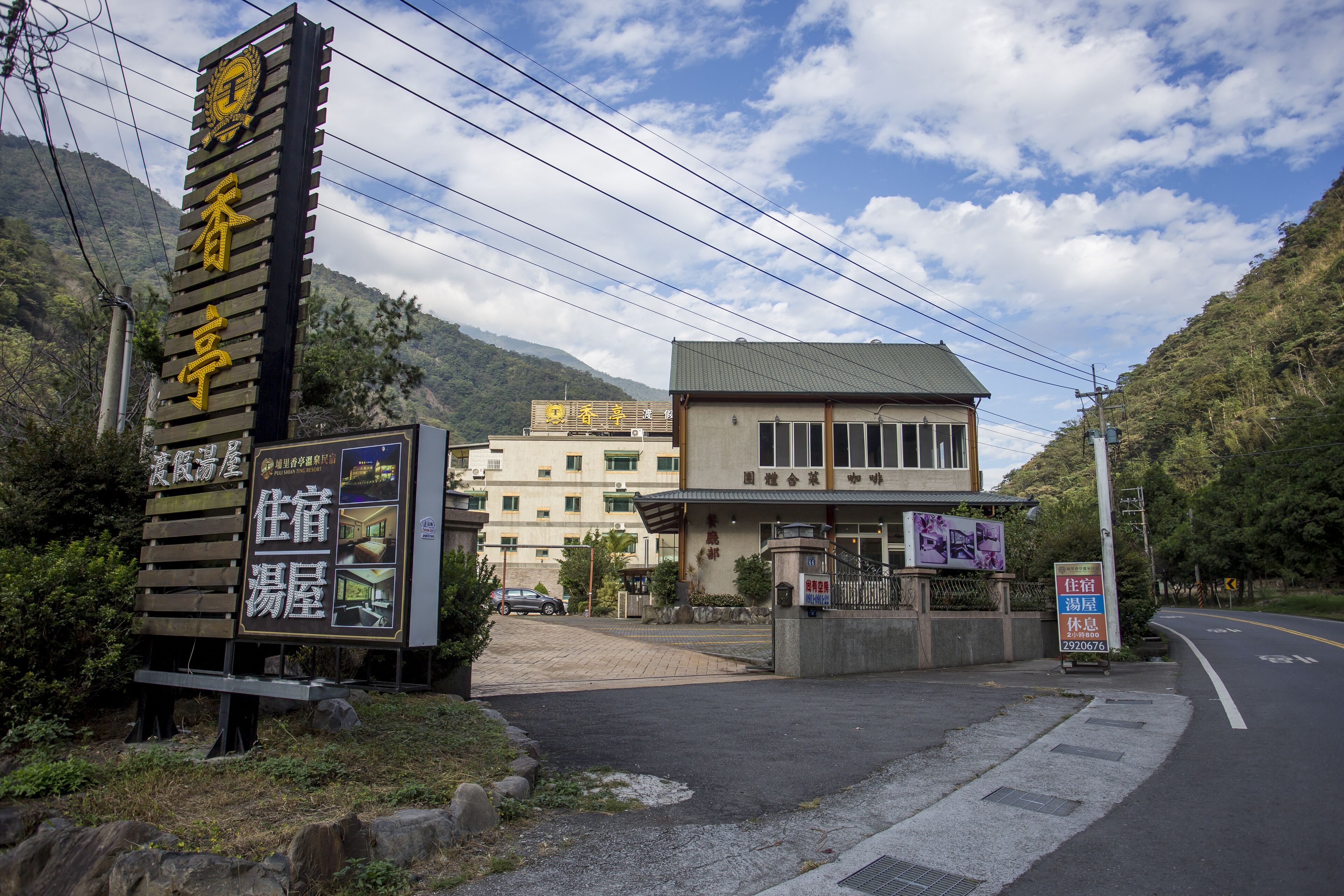 A hotel entrance with a signboard, a building with multiple floors, and a mountainous backdrop.
