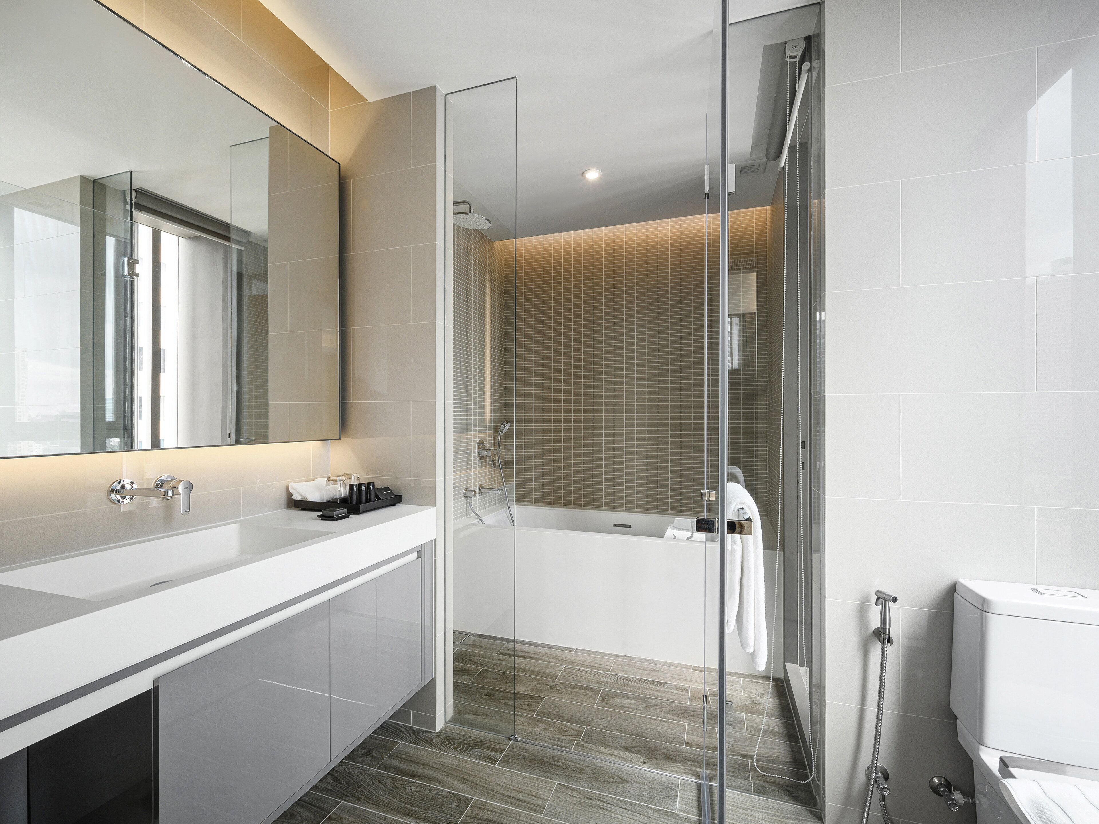 Une salle de bain moderne avec une douche à parois de verre, une baignoire blanche et un grand miroir au-dessus du meuble-lavabo.