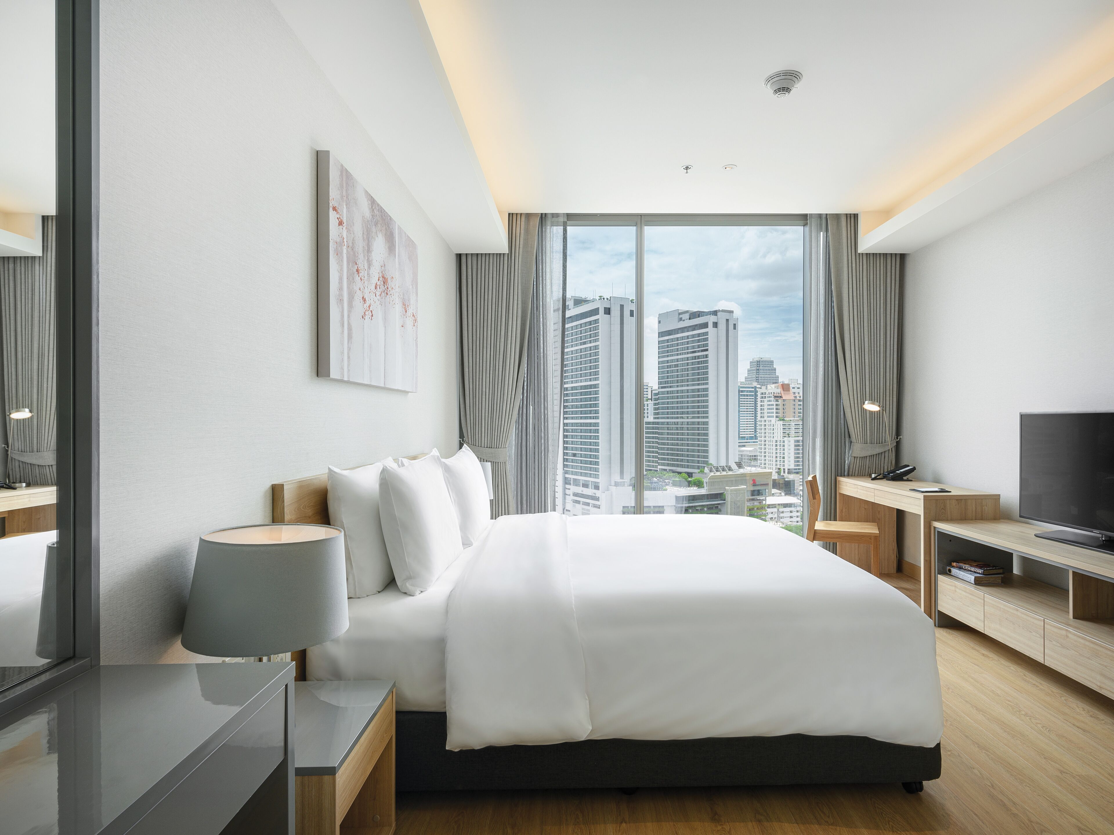 Une chambre d’hôtel moderne, dotée d’un grand lit, d’un bureau, d’une télévision et offrant une vue sur les bâtiments de la ville.
