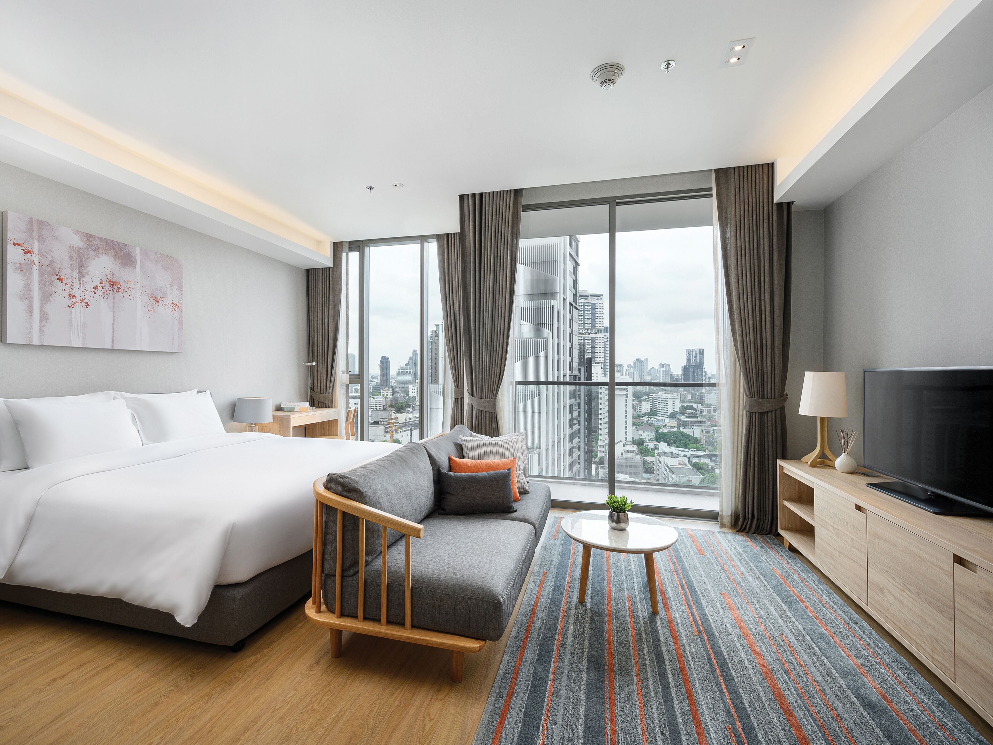 Une chambre d’hôtel moderne dotée d’un grand lit, d’un canapé, d’une télévision et offrant une vue sur la ville.