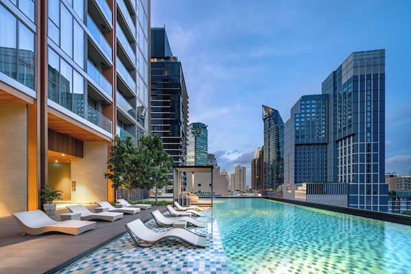 A rooftop pool with lounge chairs, a covered seating area, and modern high-rise buildings in the background. - Oakwood Suites Bangkok (Bangkok)