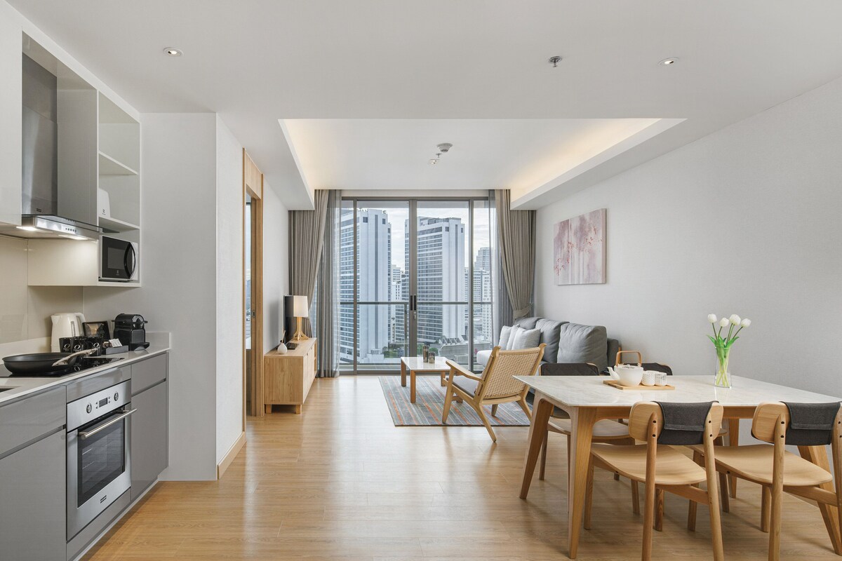 Una cocina moderna con microondas, estufa y horno, un comedor con mesa y sillas, y un amplio ventanal con vista a la ciudad.