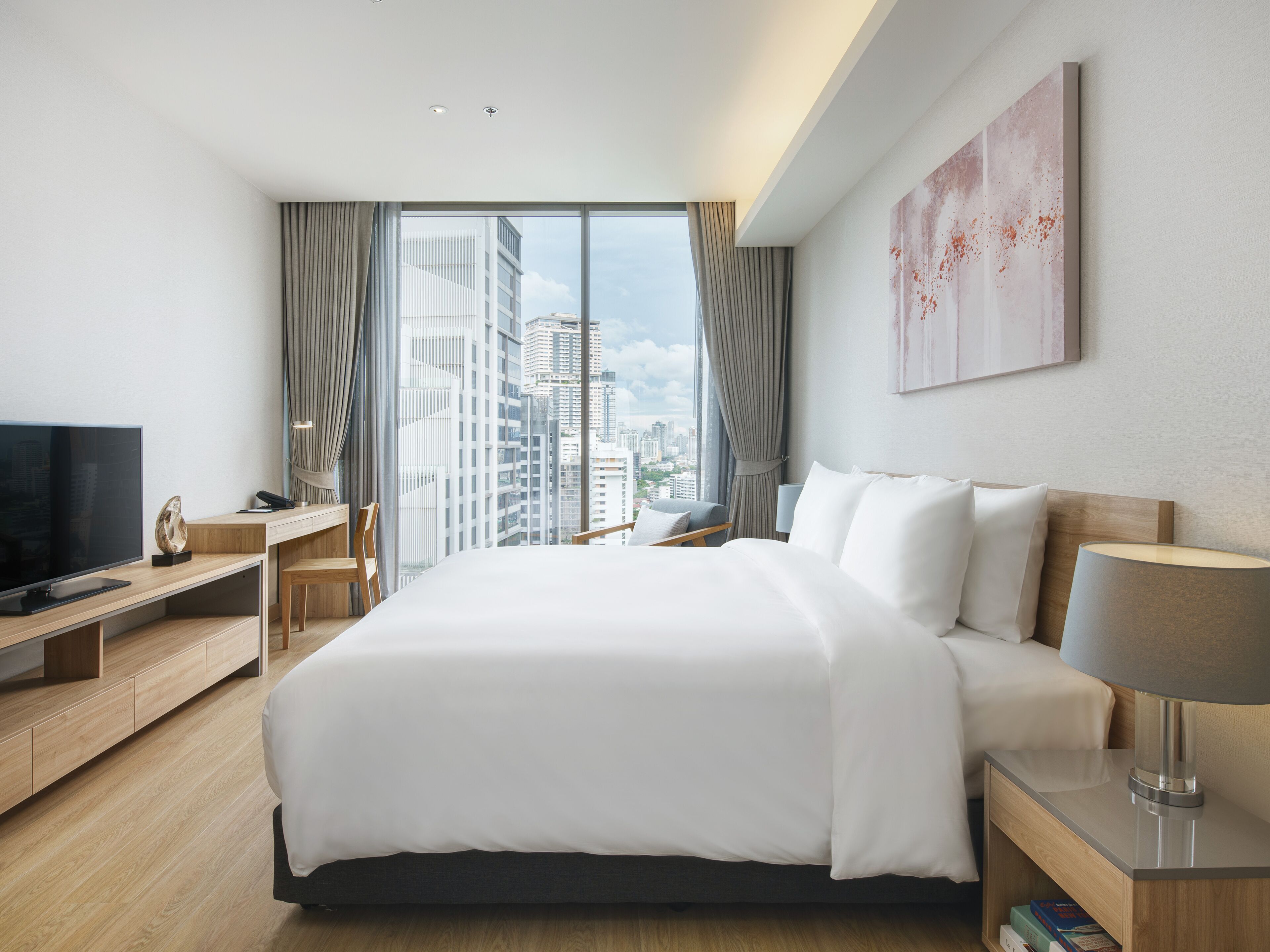 Une chambre d’hôtel moderne, dotée d’un grand lit, d’une télévision, d’un bureau et offrant une vue sur le paysage urbain.