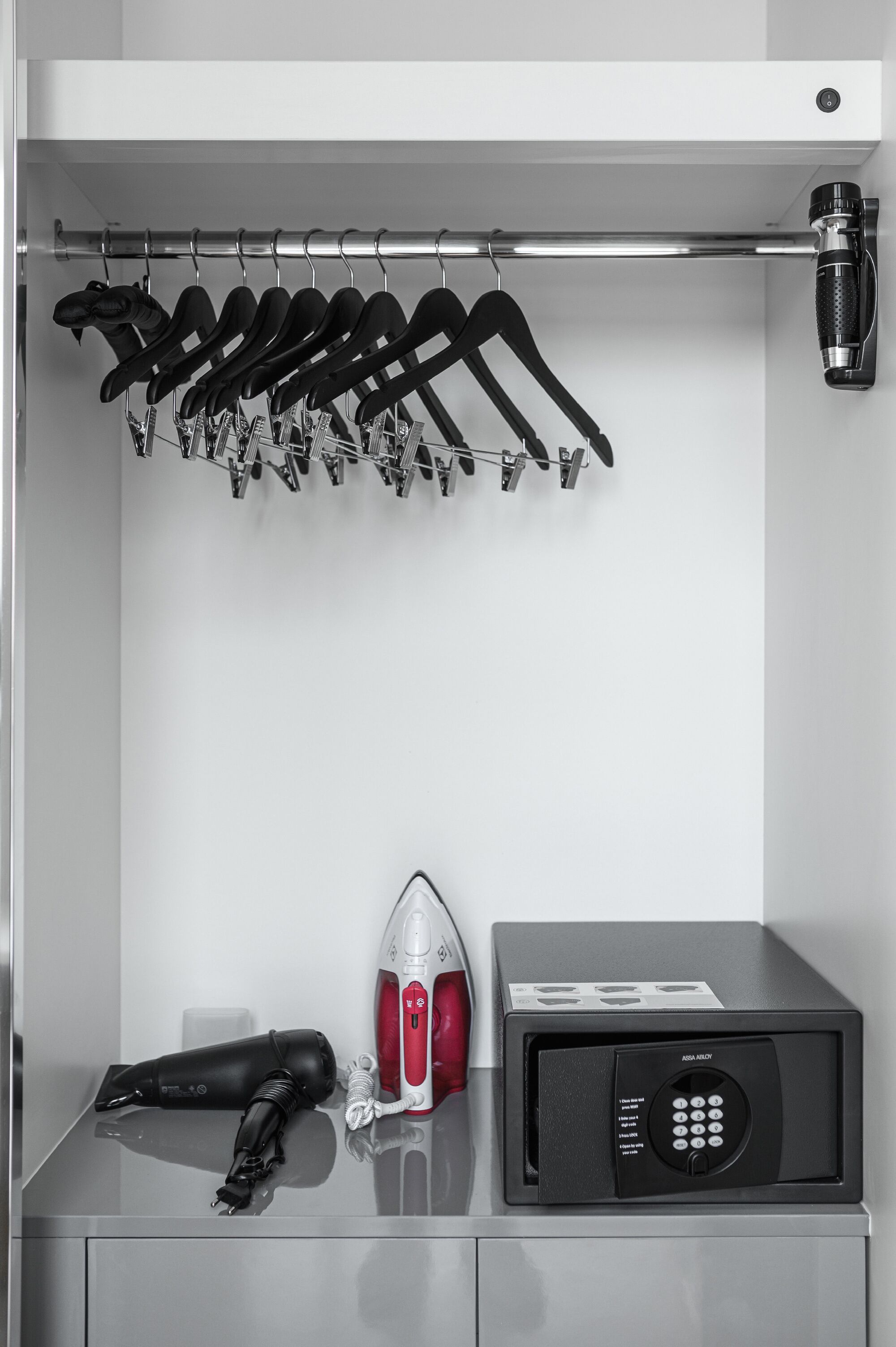 A closet with a hanging rack, an iron, and a microwave.