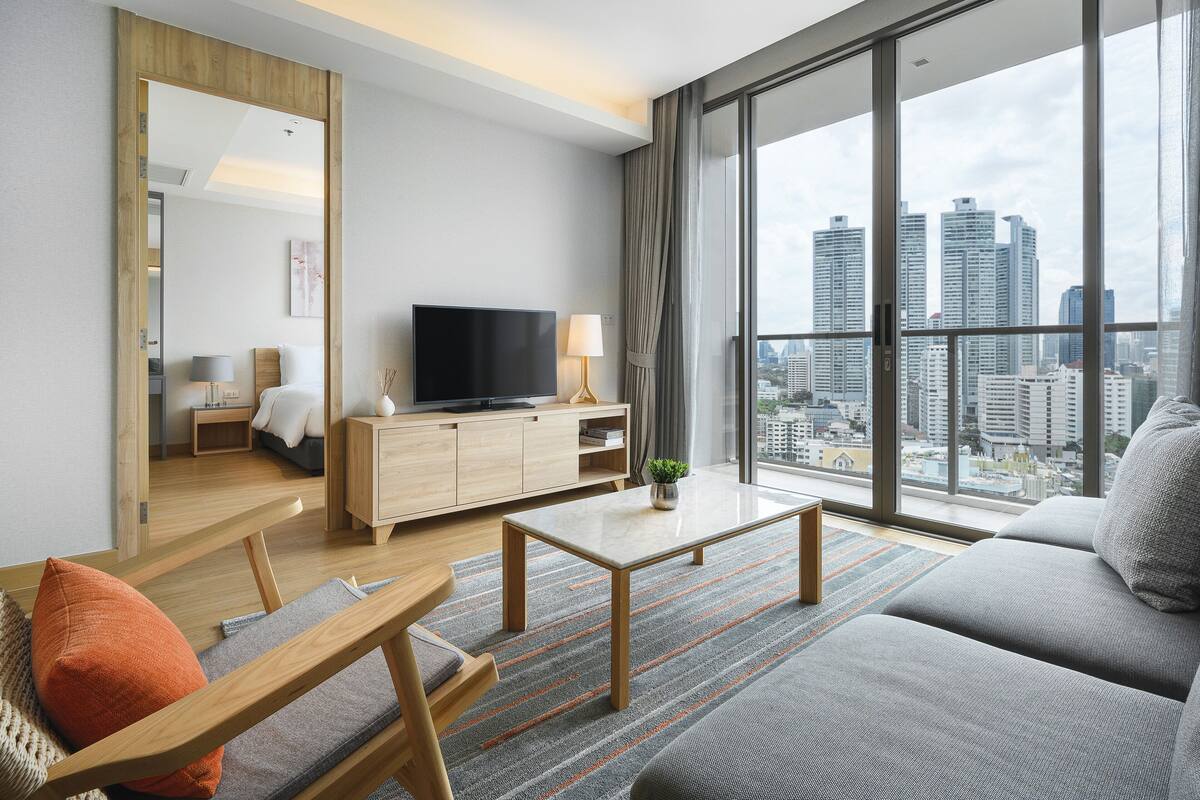 Ein modernes Wohnzimmer mit großem Fernseher, Holzmöbeln und Blick auf die Stadt.