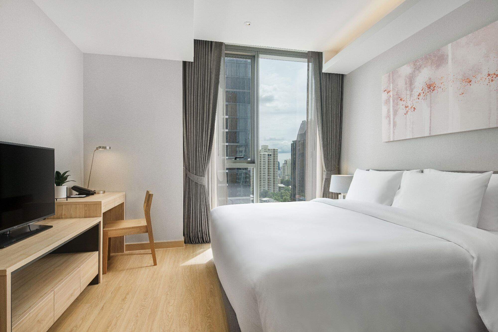 A hotel room with a bed, a desk with a TV, a chair, a window with curtains, and a city view.