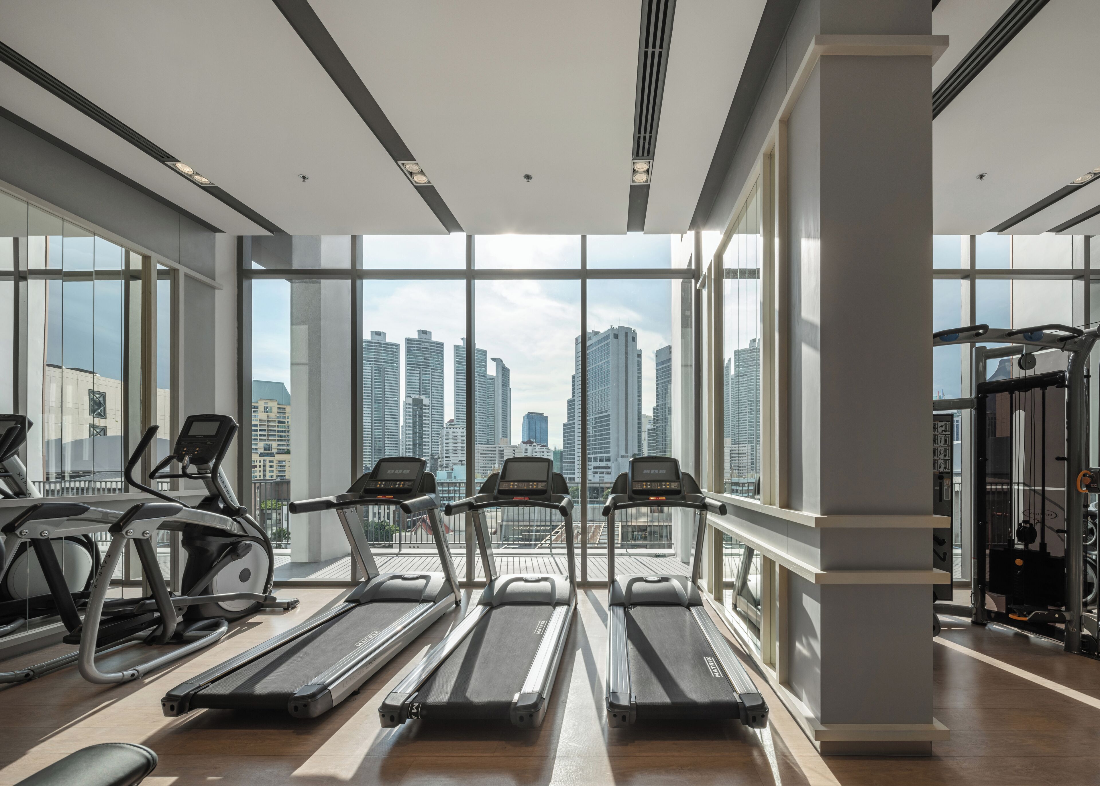 Un gimnasio con cintas de correr, bicicletas estáticas y vistas a la ciudad.