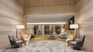 Een hotel lobby met een hoge plafond, houten lambrisering en een centraal zithoek met twee stoelen en een kleine tafel.