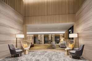 A hotel lobby with a high ceiling, wooden paneling, and a central seating area with two chairs and a small table. - Oakwood Suites Bangkok (Bangkok)