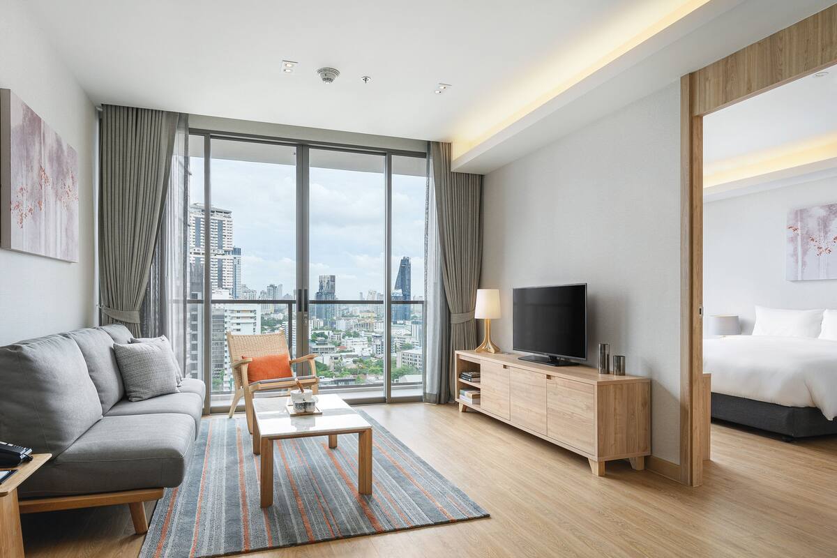 Ein modernes Hotelzimmer mit großem Fenster, einer Couch, einem Fernseher, einem Nachttisch und einem Bett.