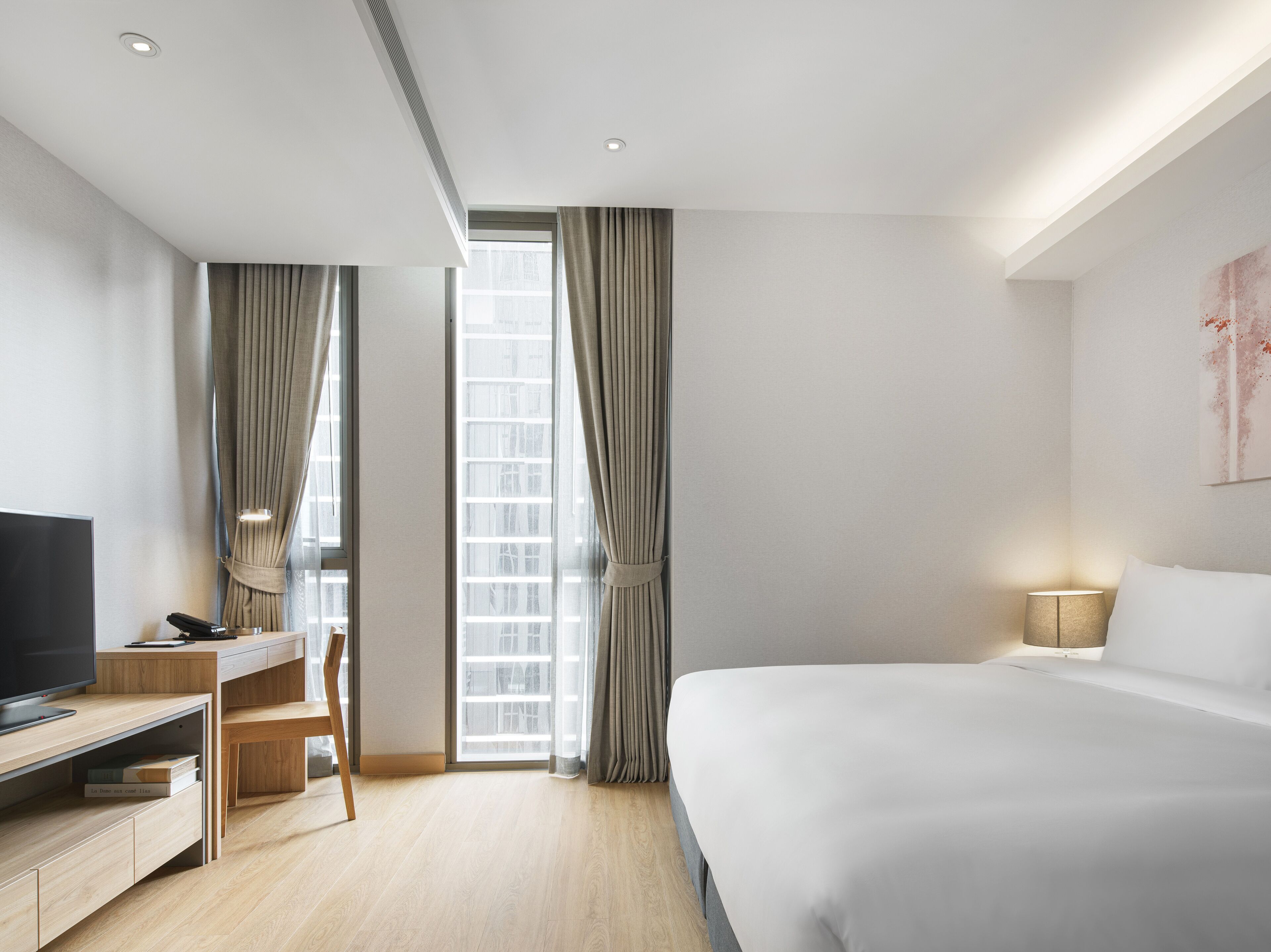 Une chambre d’hôtel moderne avec un grand lit, un bureau avec une télévision et une fenêtre avec des rideaux.