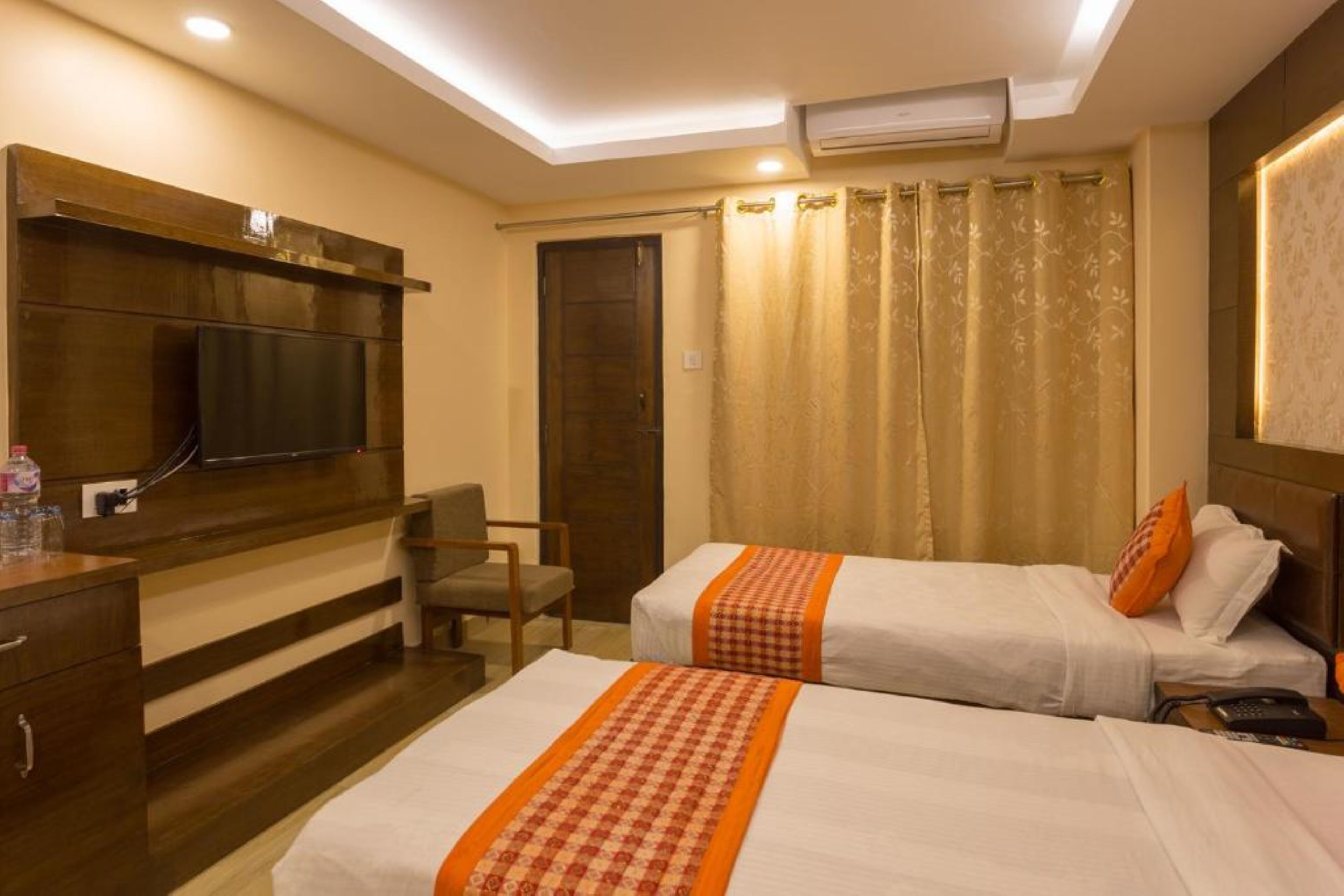 Quarto de hotel com duas camas, uma escrivaninha, uma cadeira, uma televisão e uma cortina.