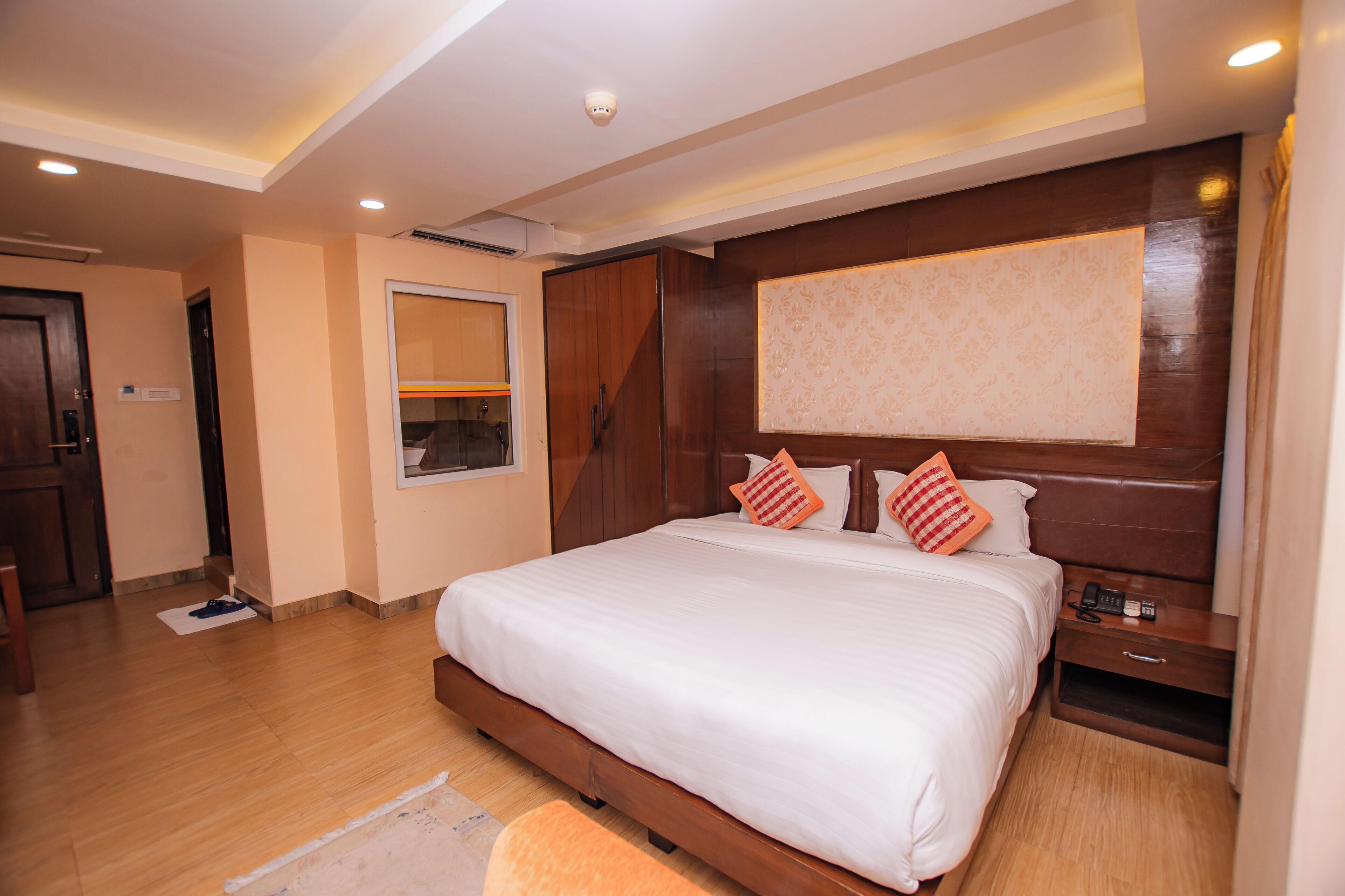 A modern hotel room with a large bed, wooden headboard, and a bedside table with a phone.