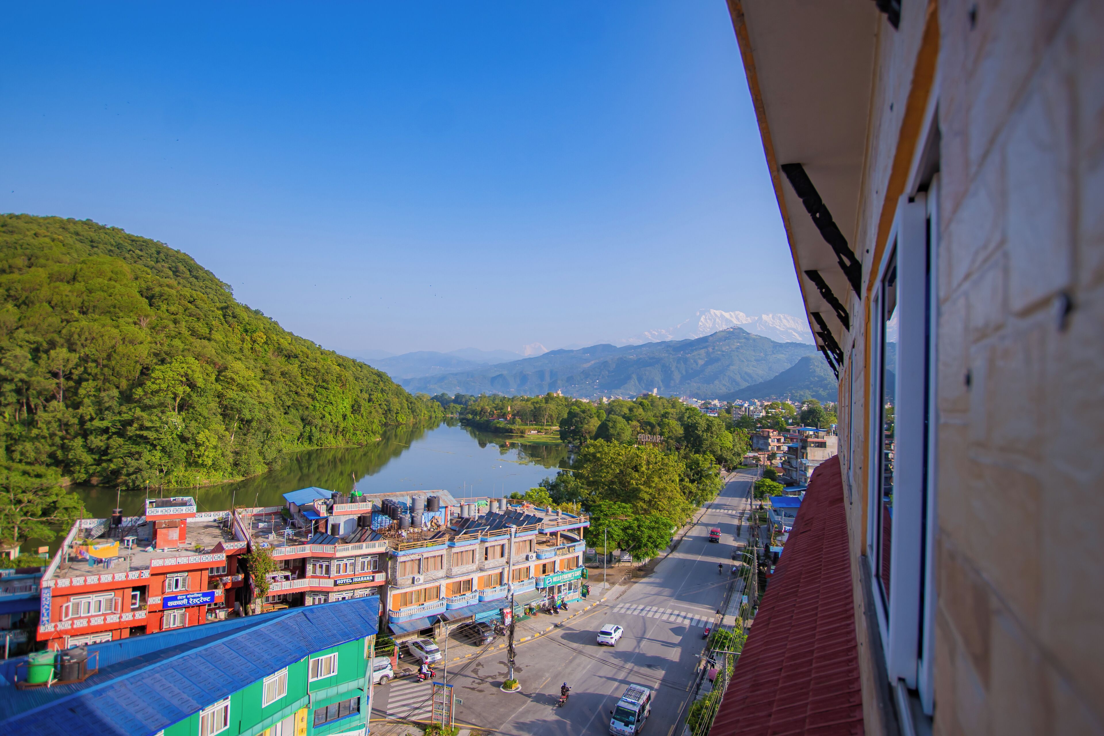 A view of a river with buildings along the riverbank, a clear sky, and mountains in the distance.