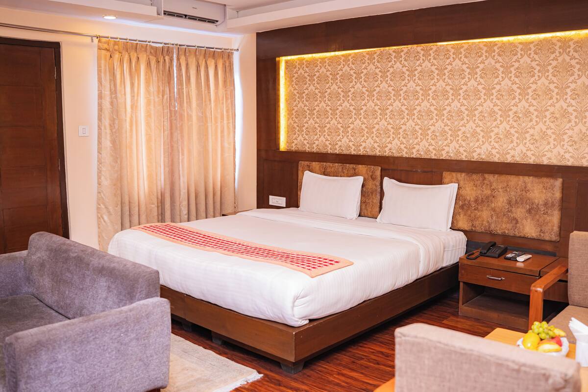 A hotel room with a large bed, a wooden headboard, a nightstand with a phone, and a seating area with two chairs.