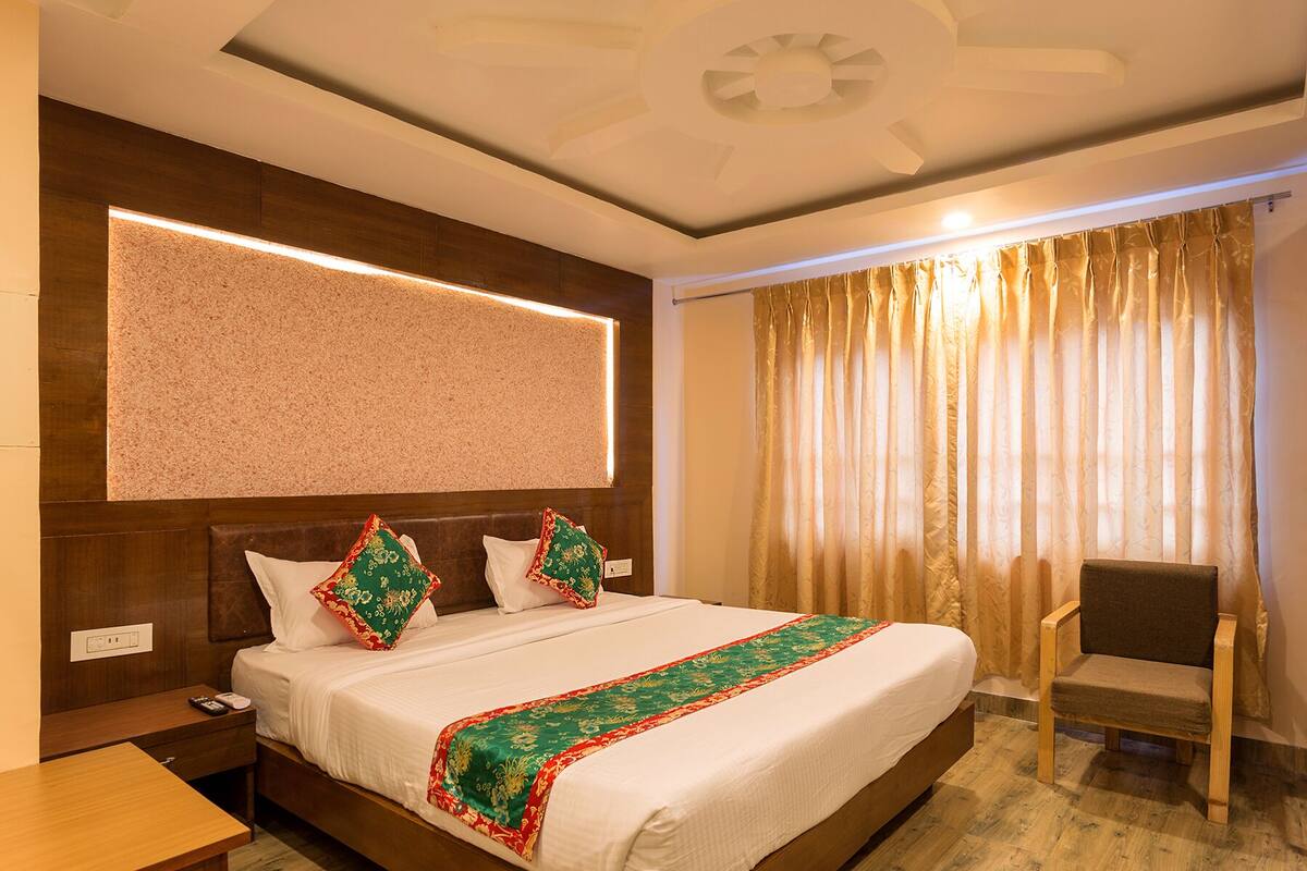 A hotel room with a large bed, a wooden headboard, a bedside table with a phone, and a chair.