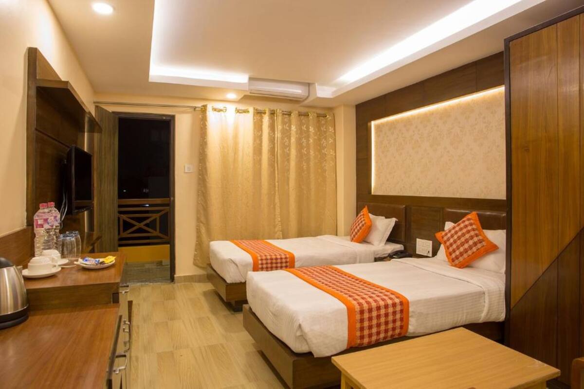 A hotel room with two beds, a wooden desk, a minibar, and a television.