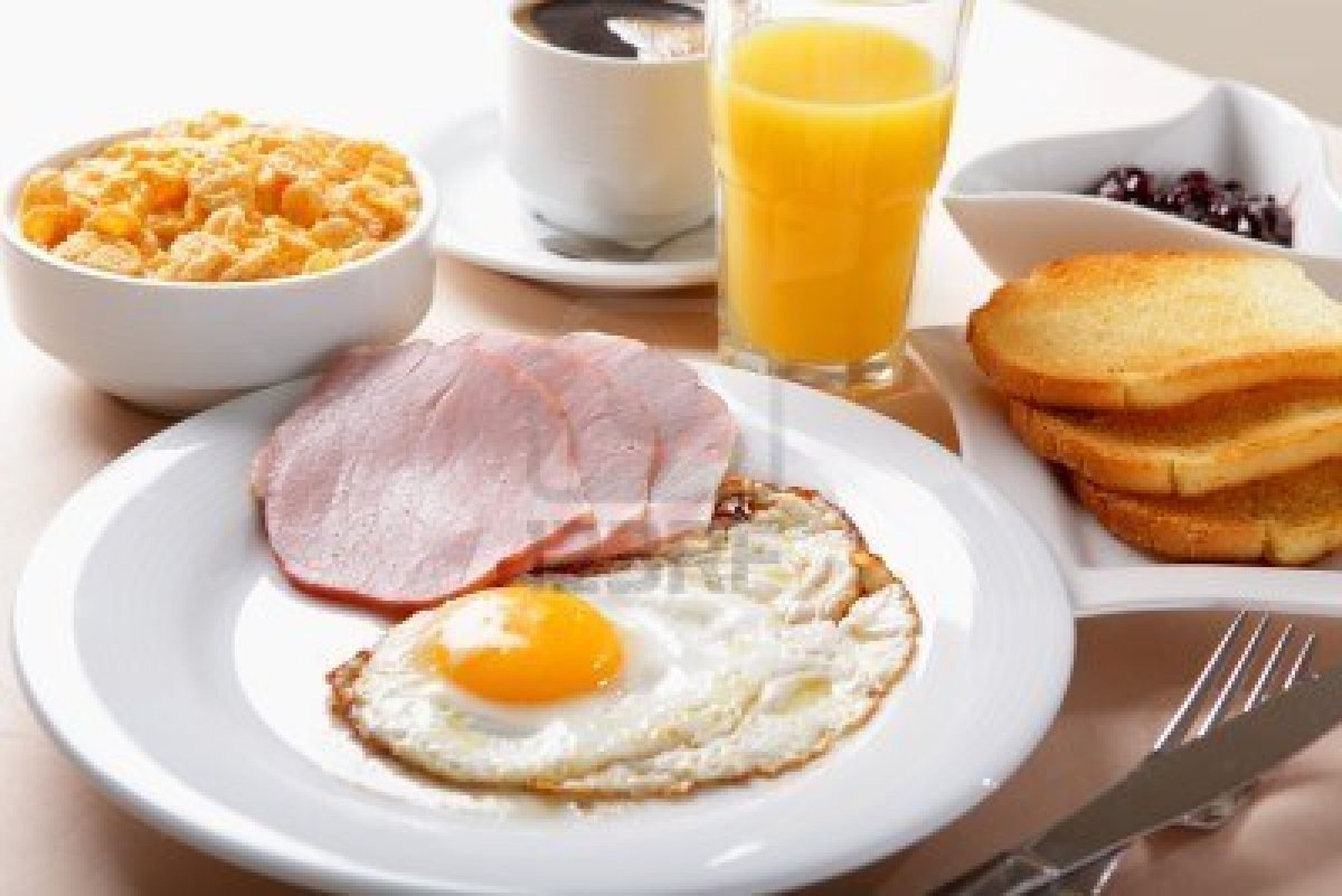 Un plato de desayuno con jamón, un huevo, tostadas y un vaso de jugo de naranja.