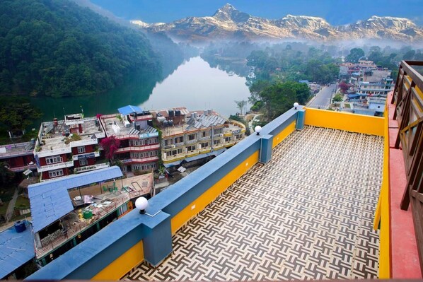 A hotel with a terrace overlooking a lake and mountains.