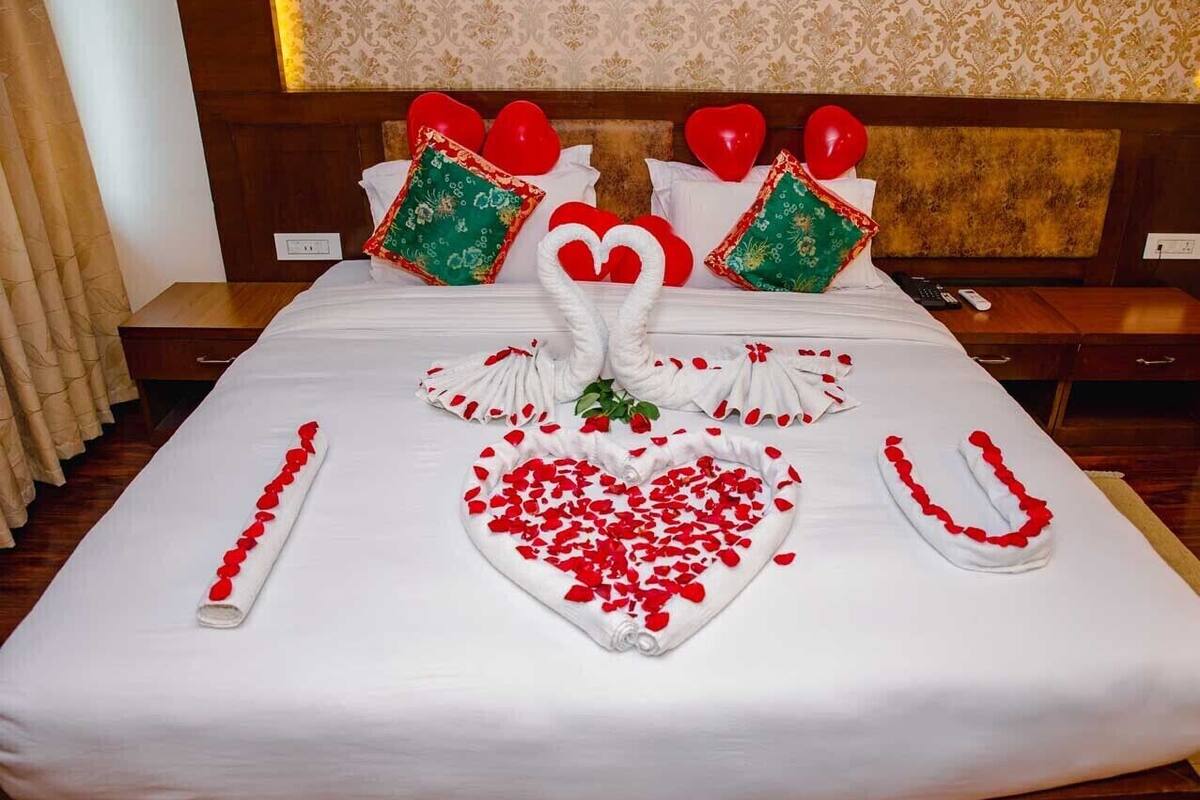 A neatly made bed with a heart-shaped arrangement of rose petals and a swan-shaped centerpiece.