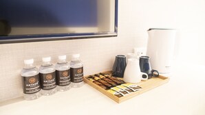 A tray with bottled beverages, coffee mugs, and tea packets on a hotel room counter. - Hatago+  The Alley (Taipei)