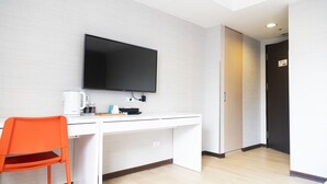 A hotel room with a white desk, a flat-screen TV mounted above it, a bright orange chair, and a wooden floor. - Hatago+  The Alley (Taipei)