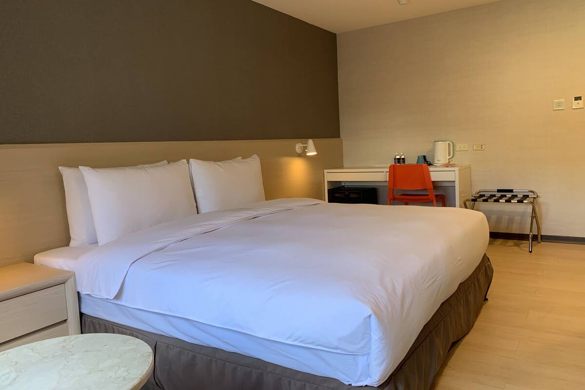 Une chambre d’hôtel avec un lit, un bureau, une chaise, une petite table et un radiateur.