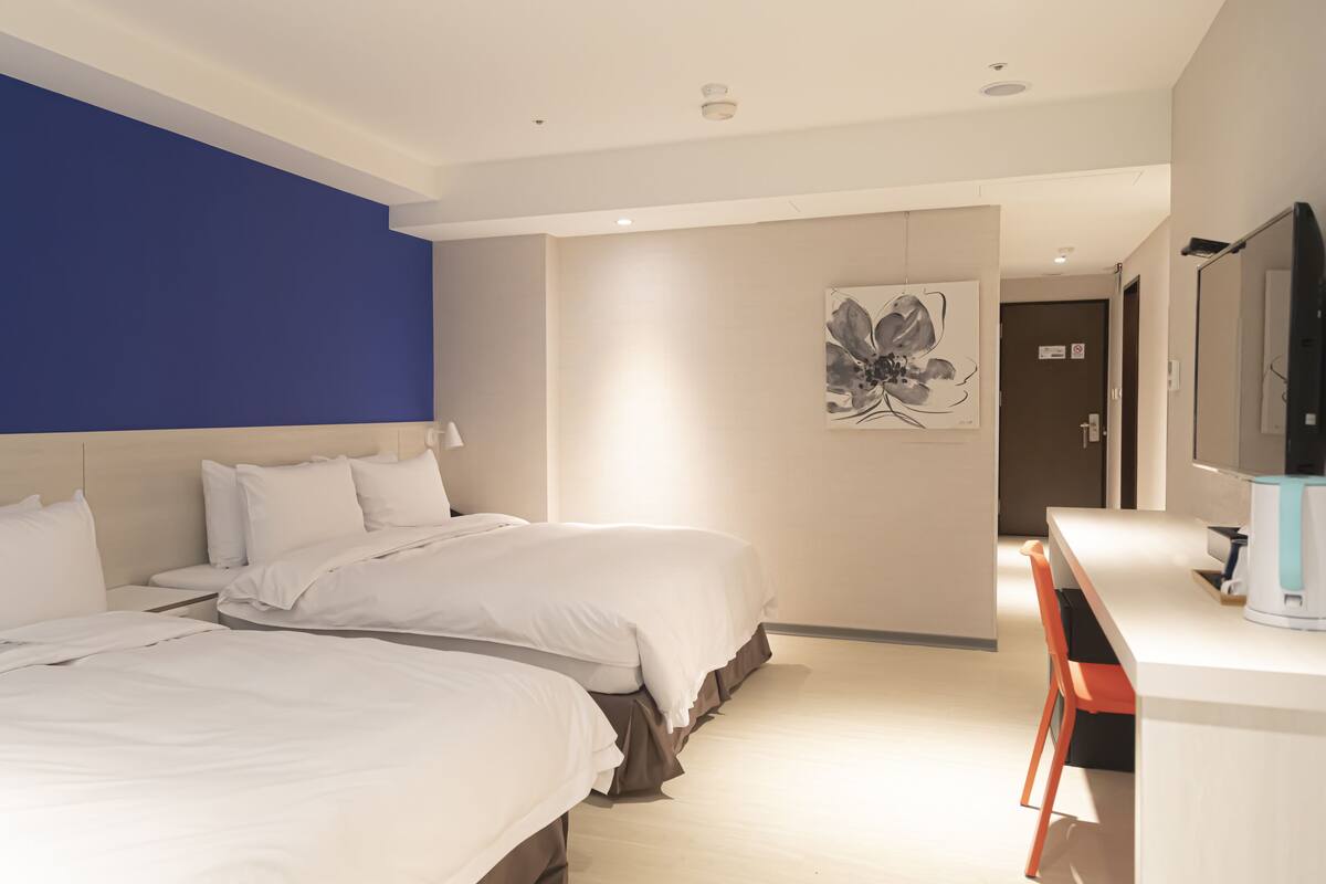 Une chambre d’hôtel avec deux lits, un bureau et un grand miroir.