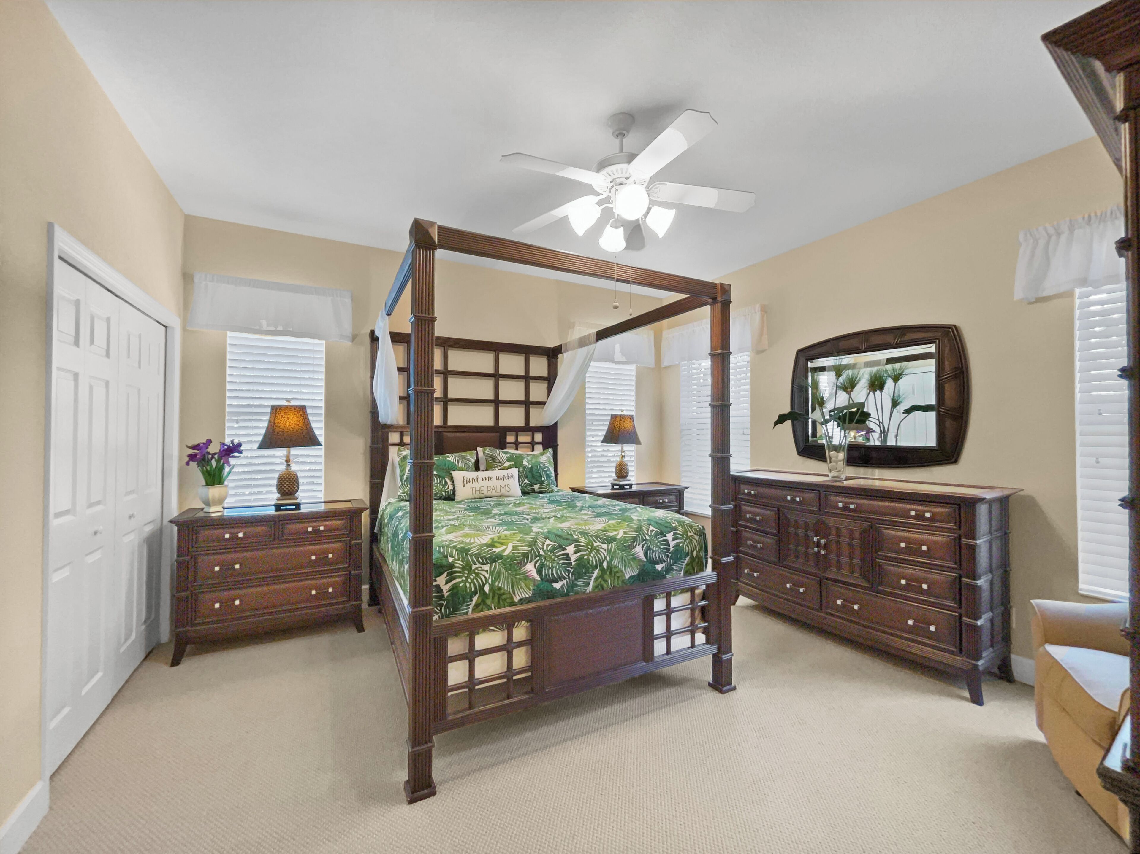 Un lit à baldaquin avec quatre poteaux, un ventilateur de plafond, un grand miroir et une commode en bois.
