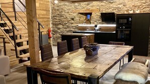 A rustic kitchen with a stone wall, wooden beams, and a dining area with a wooden table and chairs.