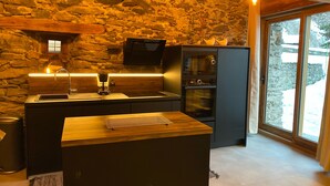 A kitchen with a stone wall, wooden beams, a modern stove, and a large window.