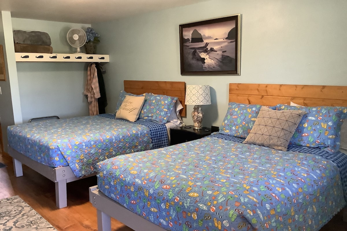 Two twin beds with matching blue bedding, a wooden headboard, a wall-mounted fan, and a framed landscape painting.