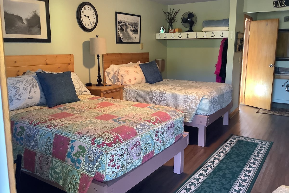 A room with two beds, a clock, and a shelf with decorative items.