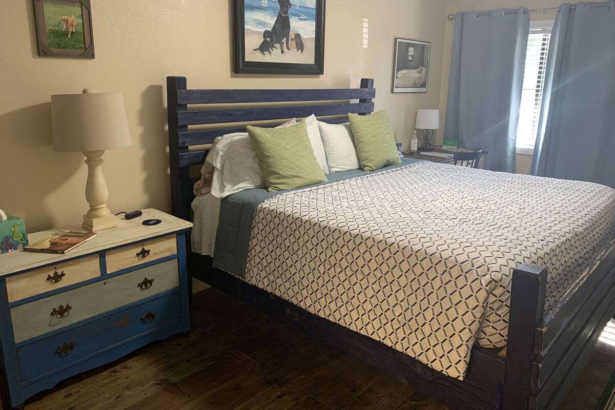 A bedroom with a wooden bed, a nightstand with a lamp, and a dresser with drawers.