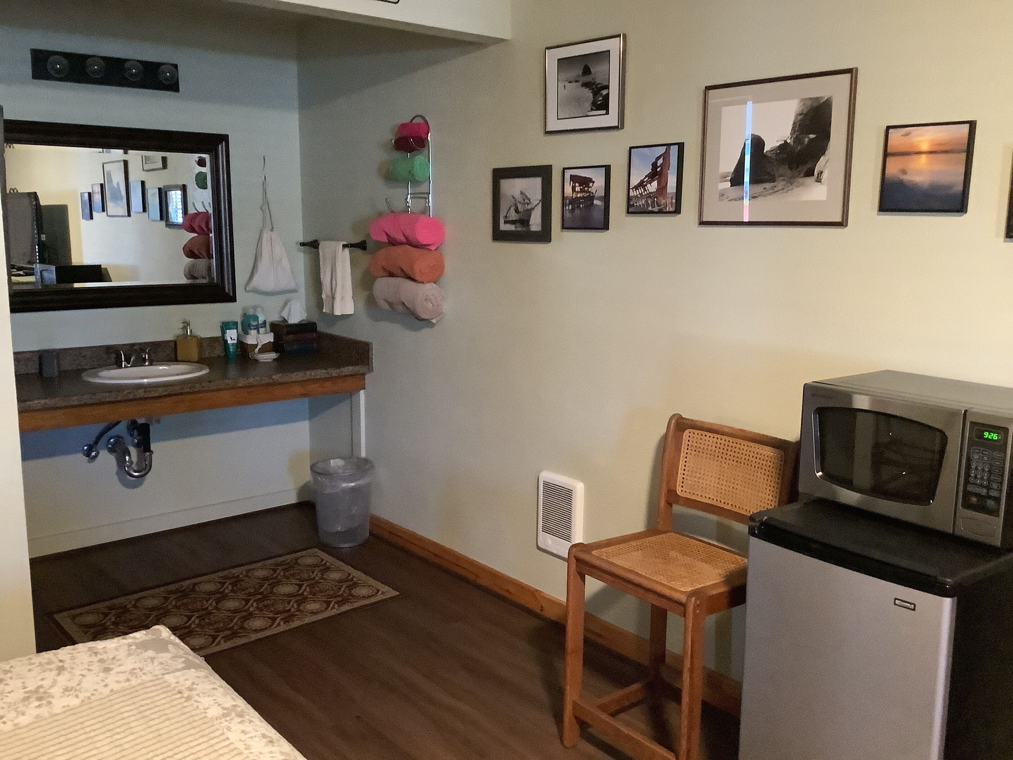 Una cocina compacta con microondas, lavabo y una pequeña silla.